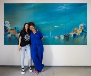 אוצרת התערוכה ולריה גסלב (מימין) עם הסטודנטית ג'ואנה סקלאר ויצירתה של סקלאר "מפרץ כחול"